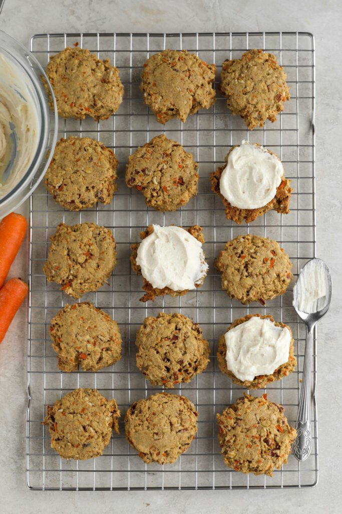 Vegan Carrot Cake cookies on a cooling rack with vegan cream cheese frosting on three and a spoon by Flora & Vino