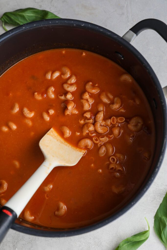 pasta in sauce in stockpot with a spatula by Flora & Vino 
