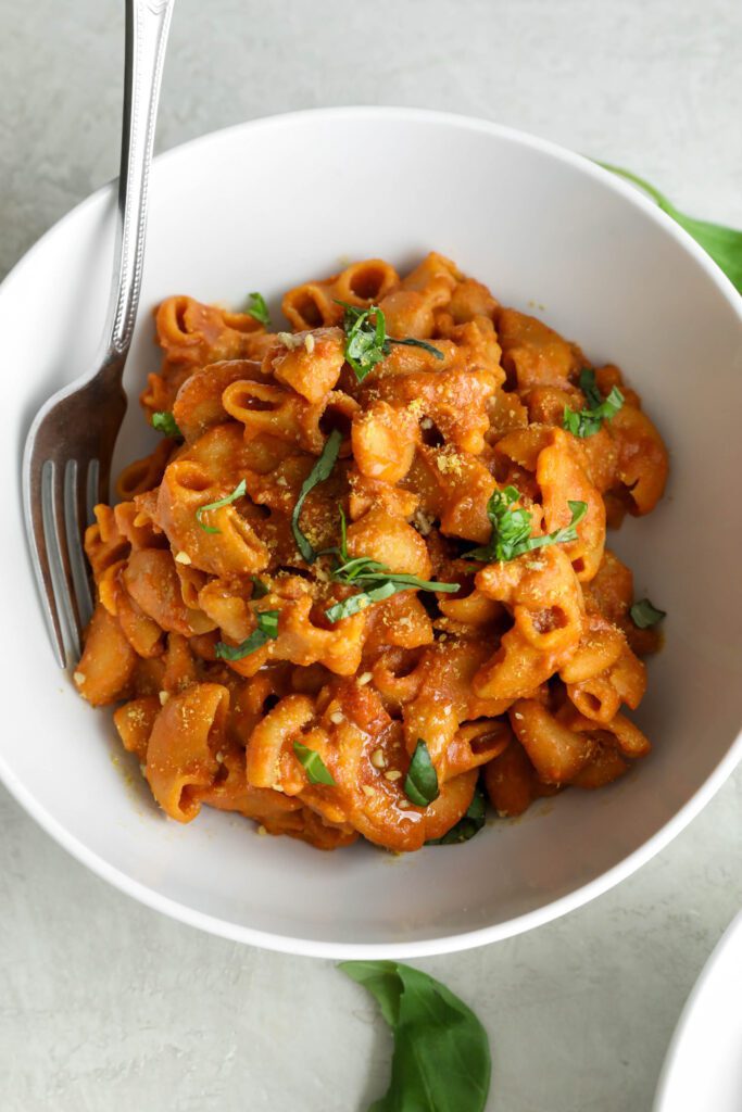 Creamy Vegan 1-Pot Pasta served in a bowl with a fork with fresh basil and vegan parmesan by Flora & Vino
