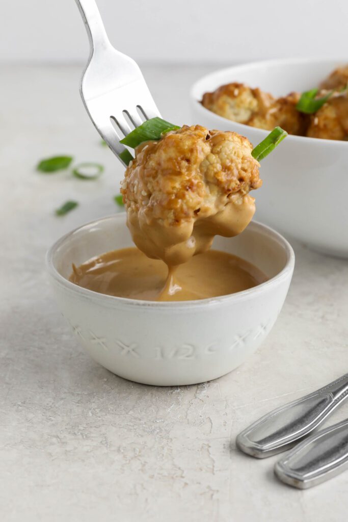 fork dipping air-fried cauliflower in Spicy SunButter sauce bowl by Flora & Vino