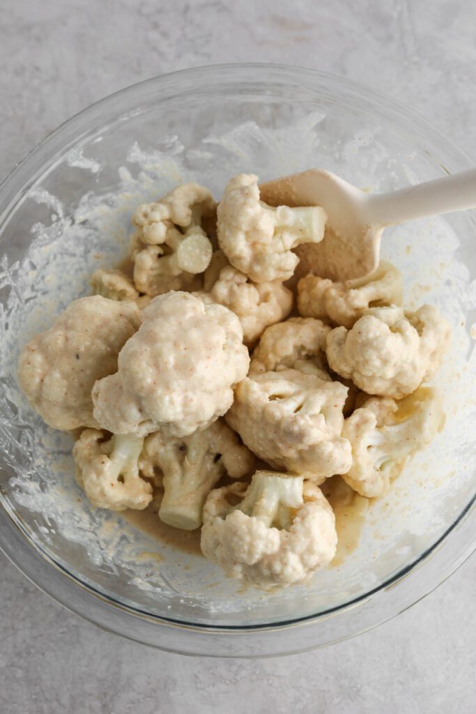 cauliflower florets mixed with batter in glass bowl with spatula by Flora & Vino