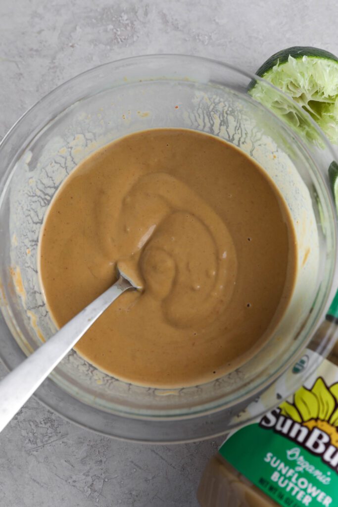 SunButter sauce mixed in glass bowl with fork with limes and SunButter on the side by Flora & Vino