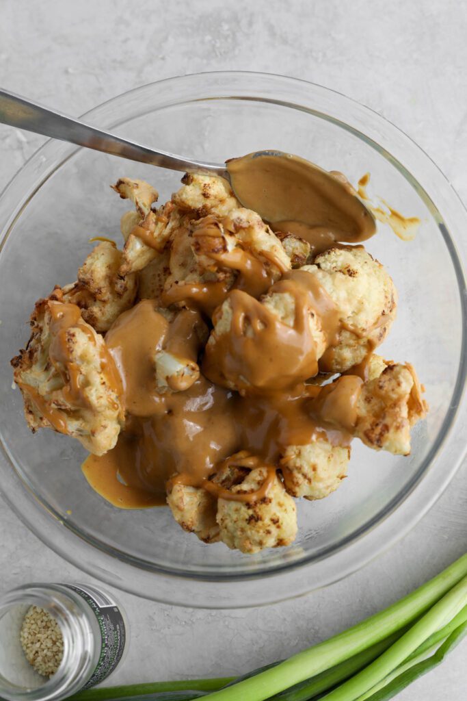 air-fried cauliflower in glass bowl topped with SunButter sauce with sesame seeds and green onion on the side by Flora & Vino