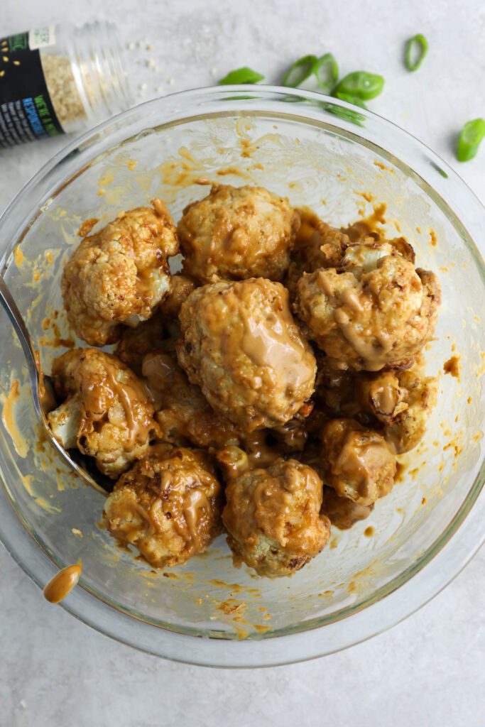 air-fried cauliflower mixed with Spicy SunButter sauce in a bowl with sesame seeds and green onion on the side by Flora & Vino