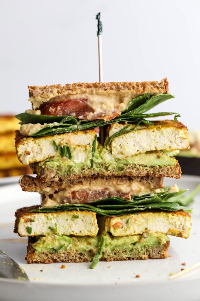 Tofu Protein Breakfast Sandwich stacked on plate with toothpick on top by Flora & Vino
