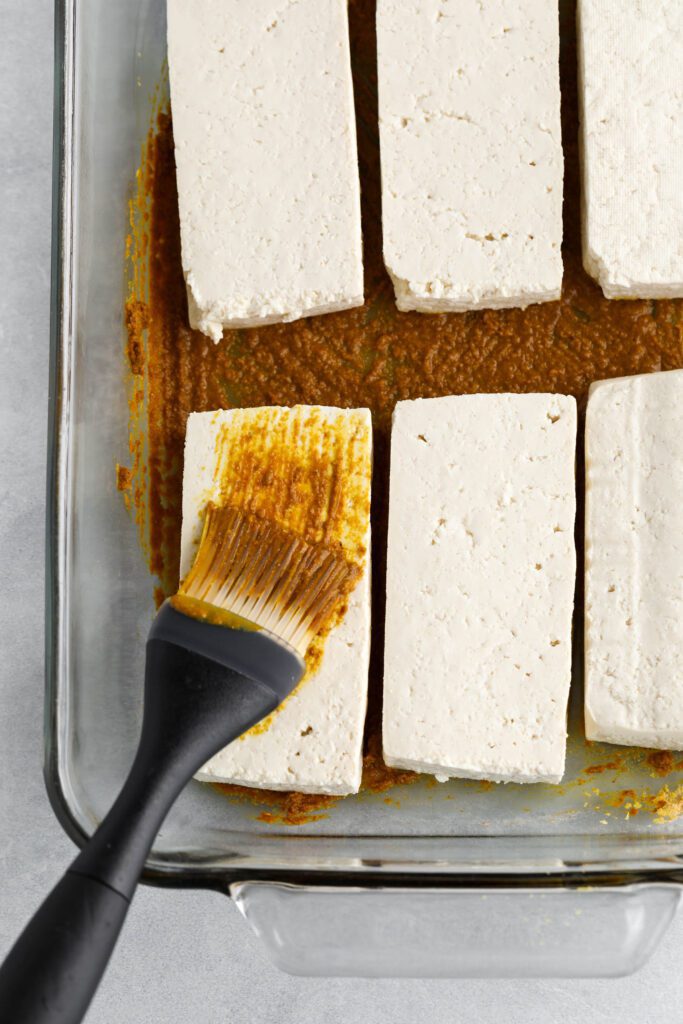 tofu cut into rectangles in baking pan brushing marinade on top by Flora & Vino