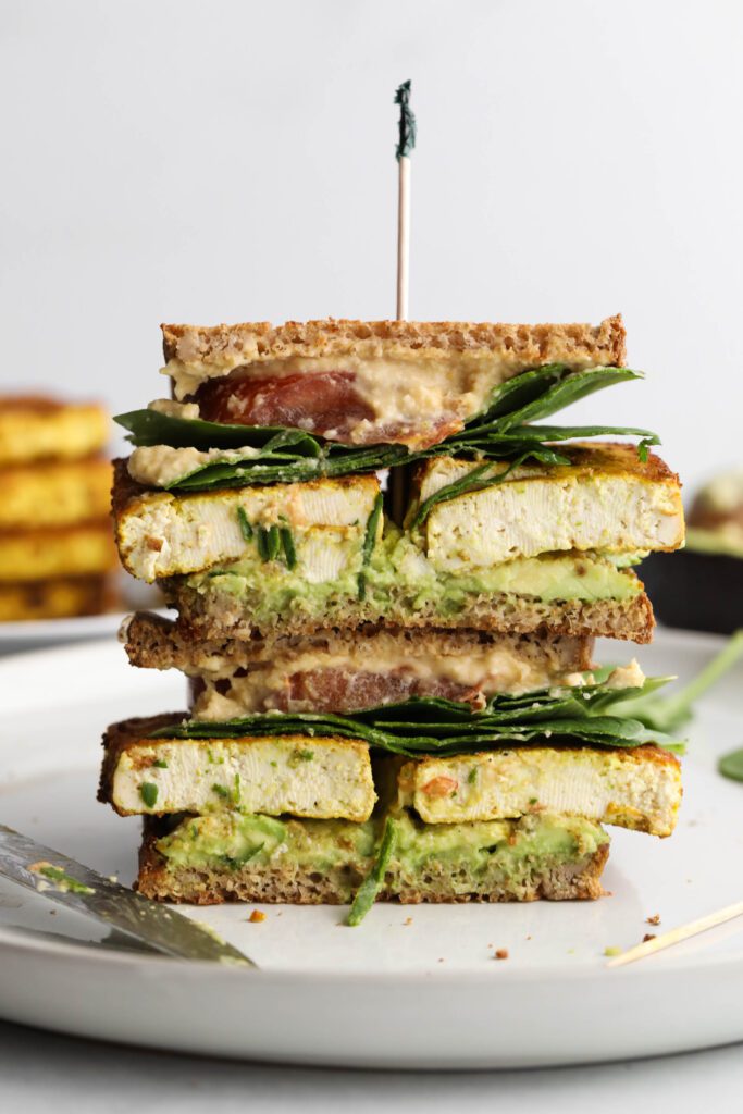 Tofu Protein Breakfast Sandwich stacked on plate with toothpick on top by Flora & Vino