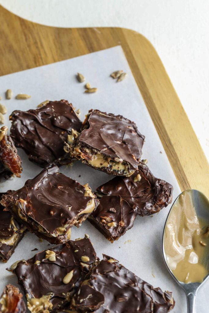 Viral Date Bark (Nut-Free!) cut into squares and served on parchment lined wooden board and spoon of SunButter by Flora & Vino