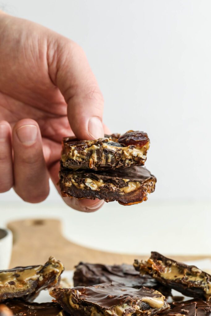 hand holding two Viral Date Bark (Nut-Free!) cut into squares by Flora & Vino