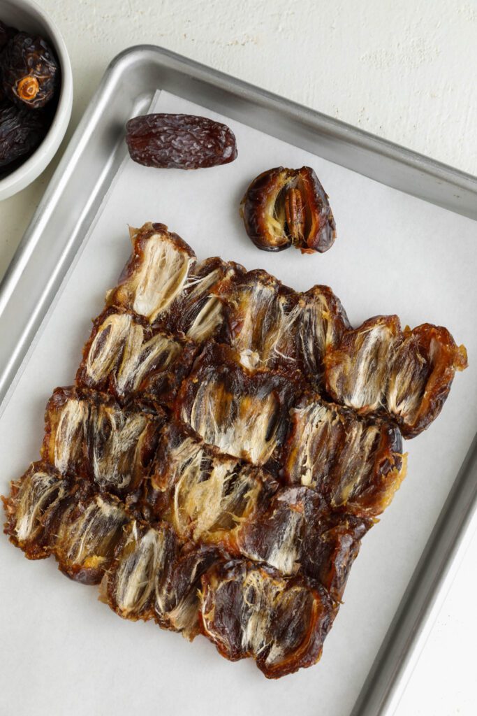 Medjool dates split open and pressed into a square on parchment lined baking sheet by Flora & Vino