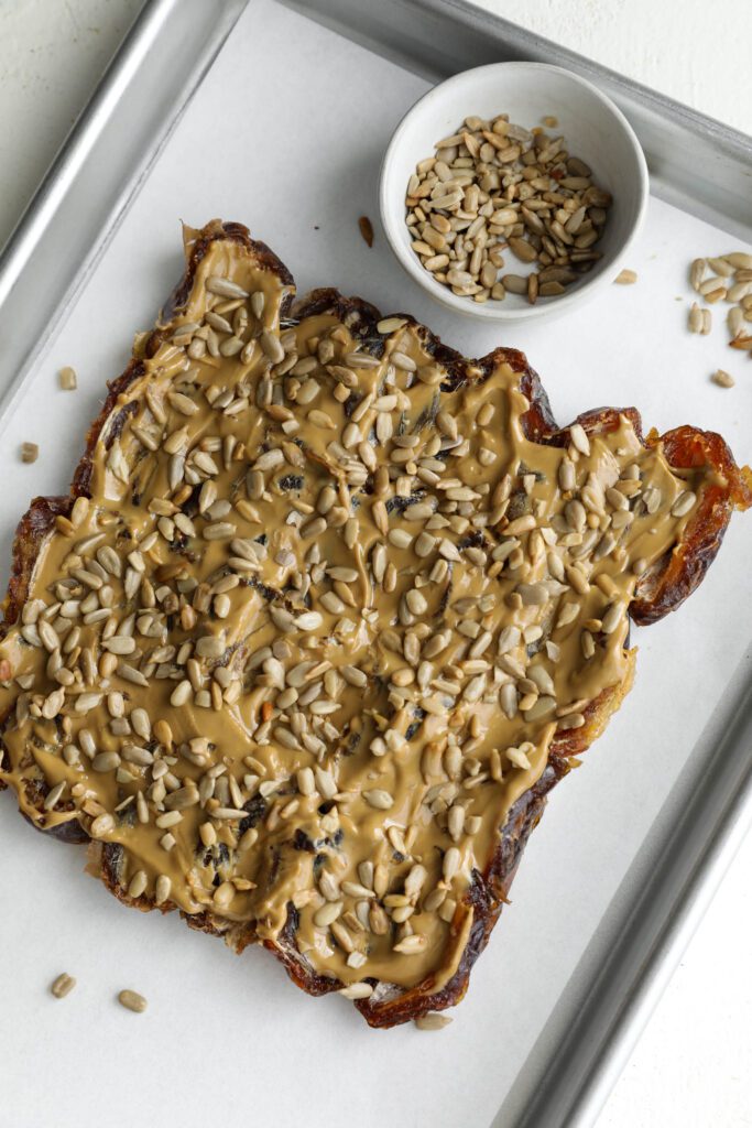 Medjool date bark process photo topped with sunflower seeds on parchment lined baking sheet with sunflower seed bowl by Flora & Vino