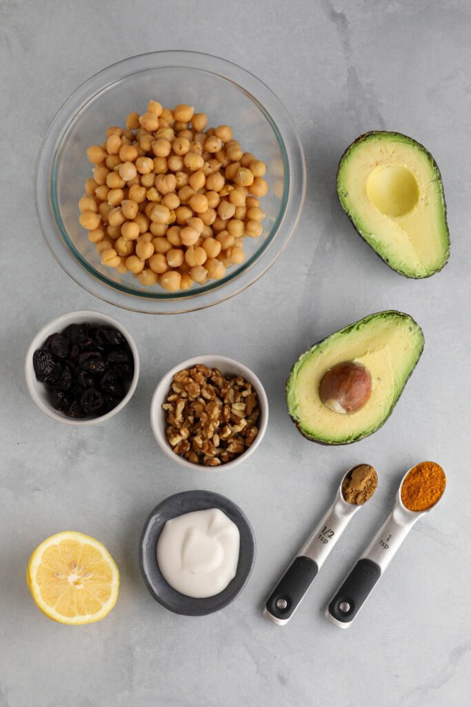chickpeas, avocado, walnuts, dried cranberries, almond milk yogurt, curry powder, cumin, and lemon on white board