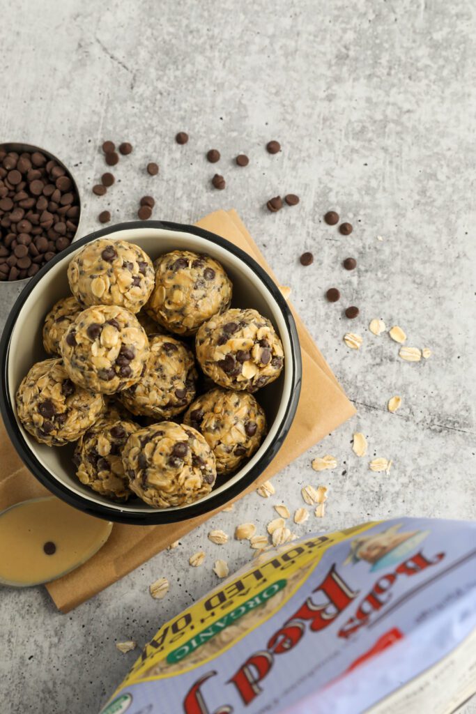 Tahini Chocolate Chip Bliss Balls served in bowl on top of parchment paper with chocolate chips and oats scattered and spoon of tahini 