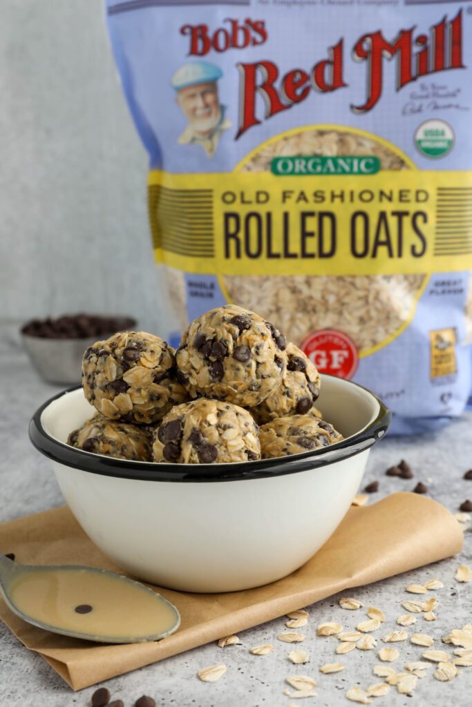 Tahini Chocolate Chip Bliss Balls served in bowl on top of parchment paper with chocolate chips and oats scattered and spoon of tahini 