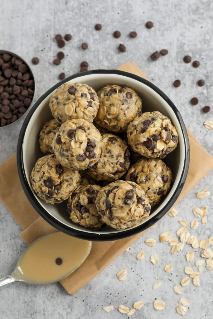Tahini Chocolate Chip Bliss Balls served in bowl on top of parchment paper with chocolate chips and oats scattered and spoon of tahini 