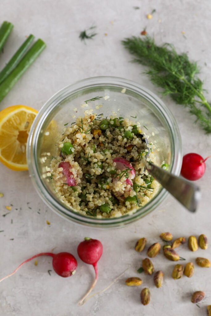 two Spring Quinoa Salad Jar mixed together and served overhead with spoon in jar and pistachios, radishes, dill, lemon, and green onion on the side