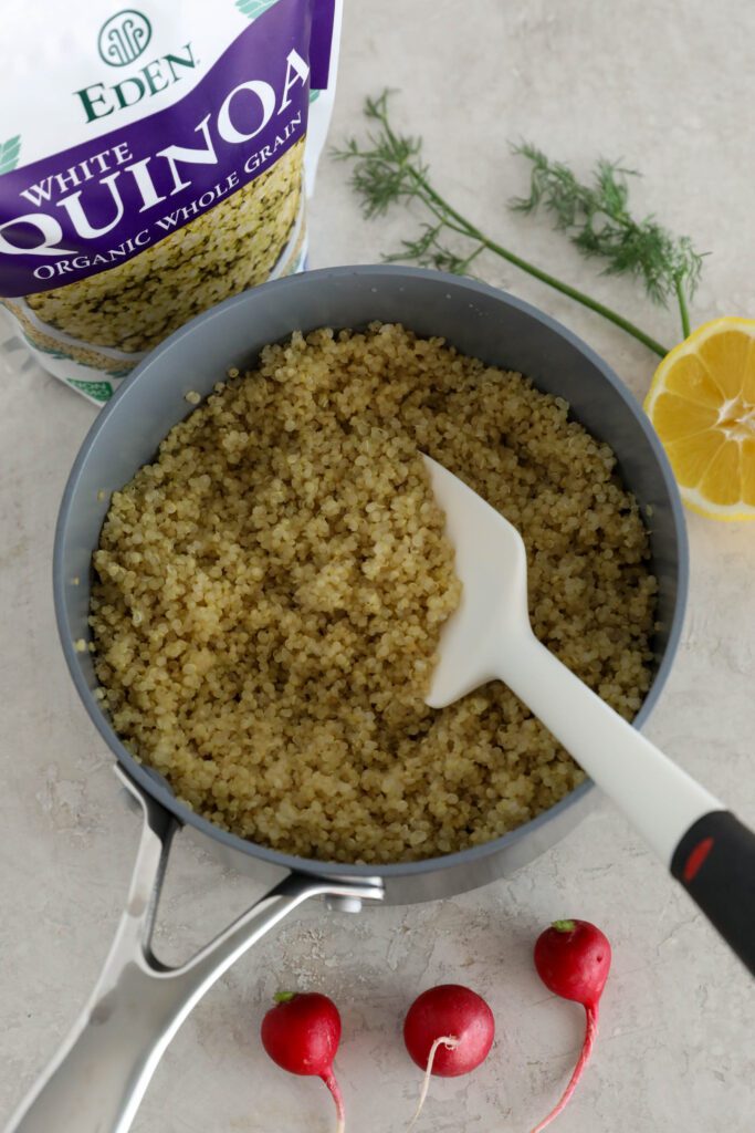 white quinoa cooked in small pot with spatula. half a lemon, radishes, fresh dill, and bag of Eden Foods quinoa is on the side