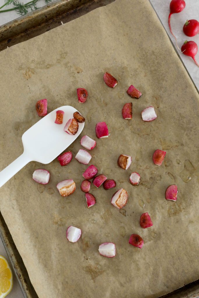 roasted radishes on parchment lined sheet pan with spatula and fresh dill and lemon on the side