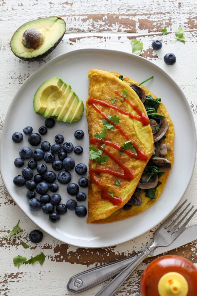 Vegan Mushroom Omelette served on plate with blueberries and avocado topped with hot sauce and cilantro 