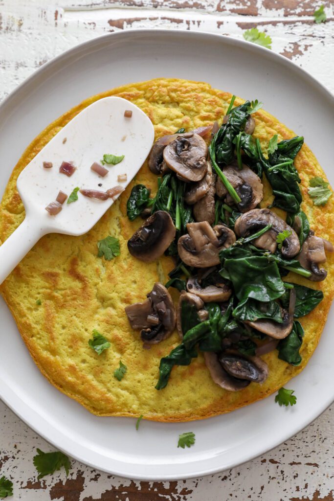 Vegan Mushroom Omelette served on plate topped with sautéed mushroom and spinach with spatula 