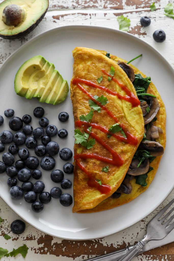 Vegan Mushroom Omelette served on plate with blueberries and avocado topped with hot sauce and cilantro 