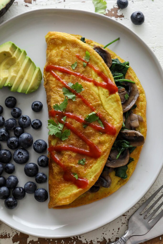 Vegan Mushroom Omelette served on plate with blueberries and avocado topped with hot sauce and cilantro 