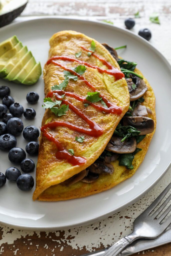 Vegan Mushroom Omelette served on plate with blueberries and avocado topped with hot sauce and cilantro 