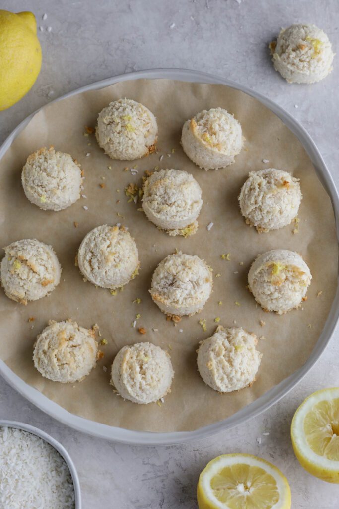 Lemon Almond Flour Macaroons on parchment lined plate with lemons and shredded coconut on the side
