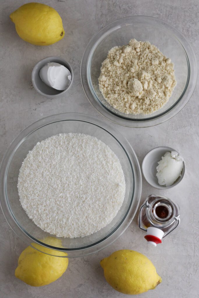 unsweetened shredded coconut, lemons, almond flour, coconut butter, coconut oil, and maple syrup on white board