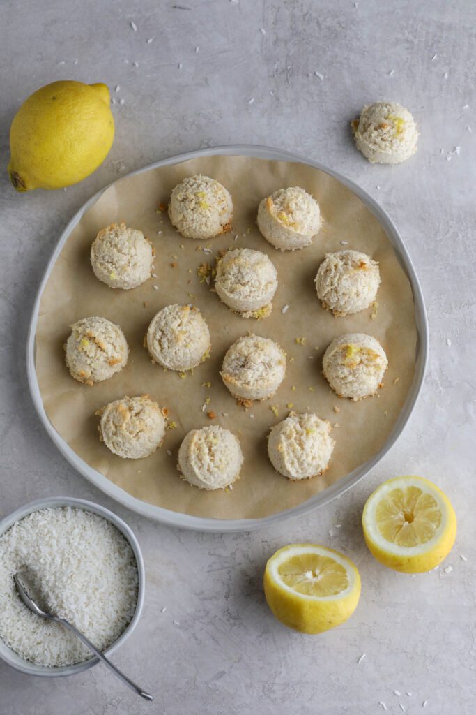 Lemon Almond Flour Macaroons on parchment lined plate with lemons and shredded coconut on the side