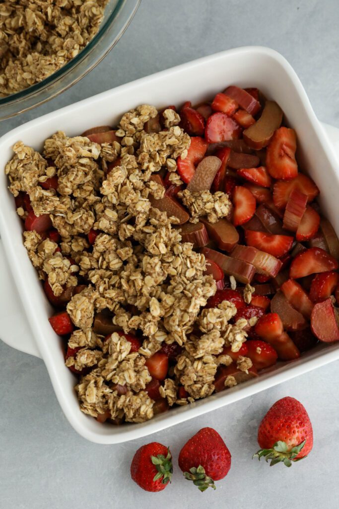 crumble topping added on top of strawberry rhubarb topping in square baking dish 