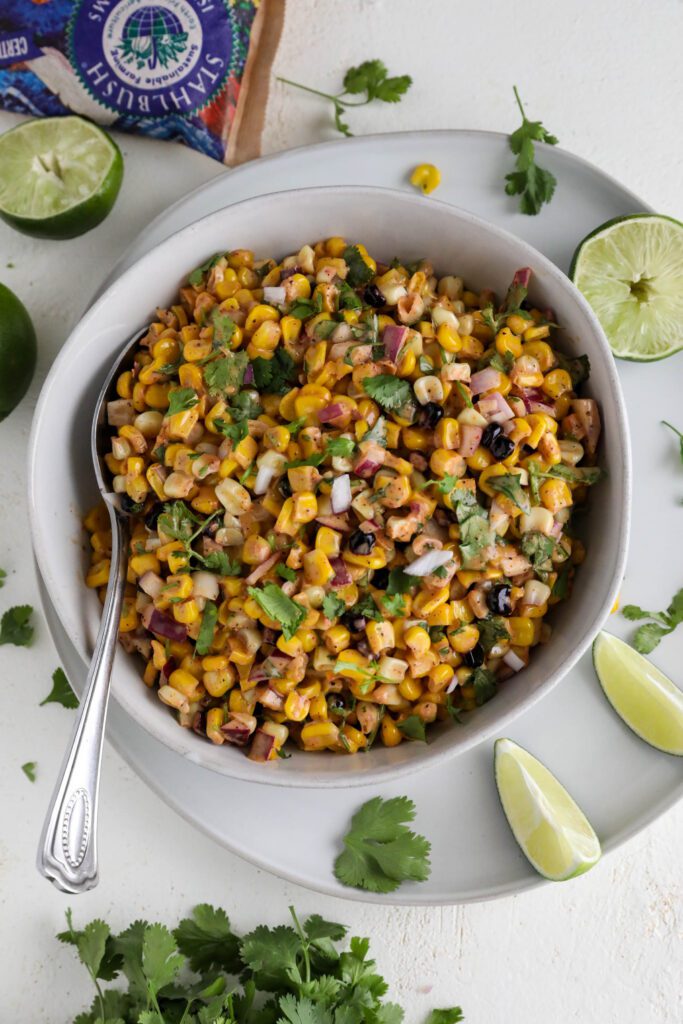 Vegan Elote Corn Salad served in bowl with spoon on plate with lime slices 
