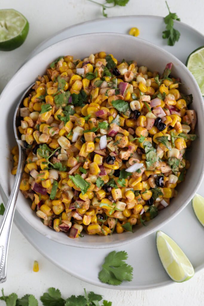 Vegan Elote Corn Salad served in bowl with spoon on plate with lime slices 