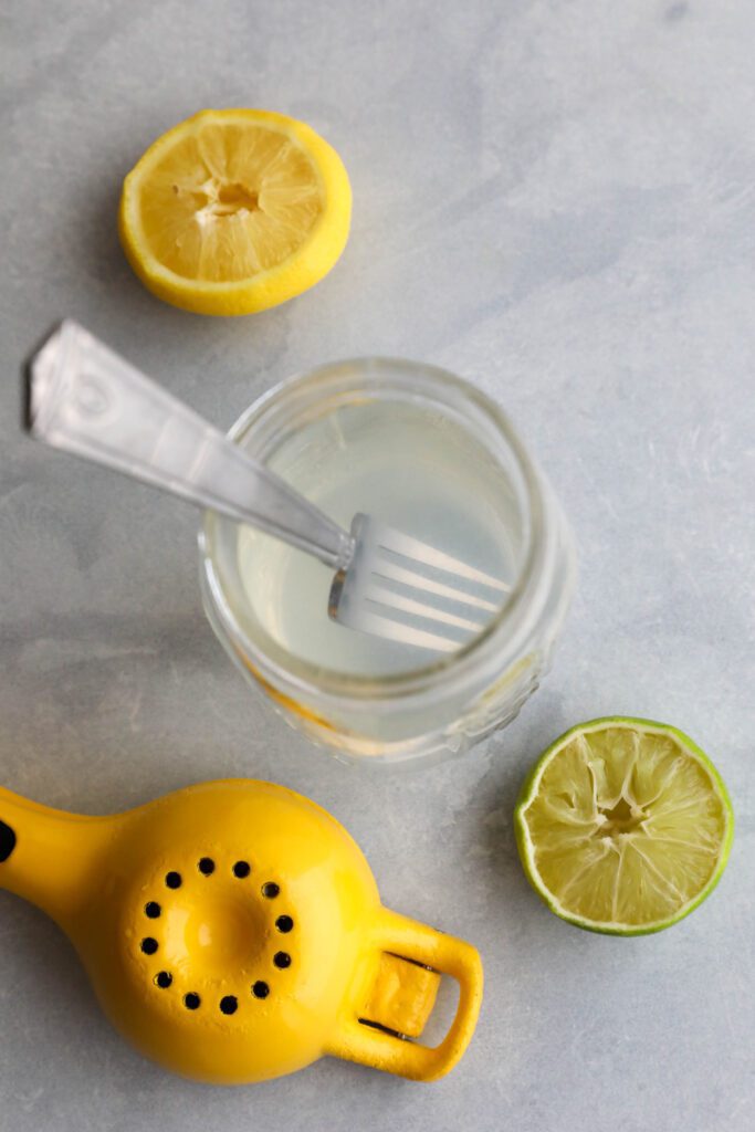 lemon and lime halves squeezed into water with fork 
