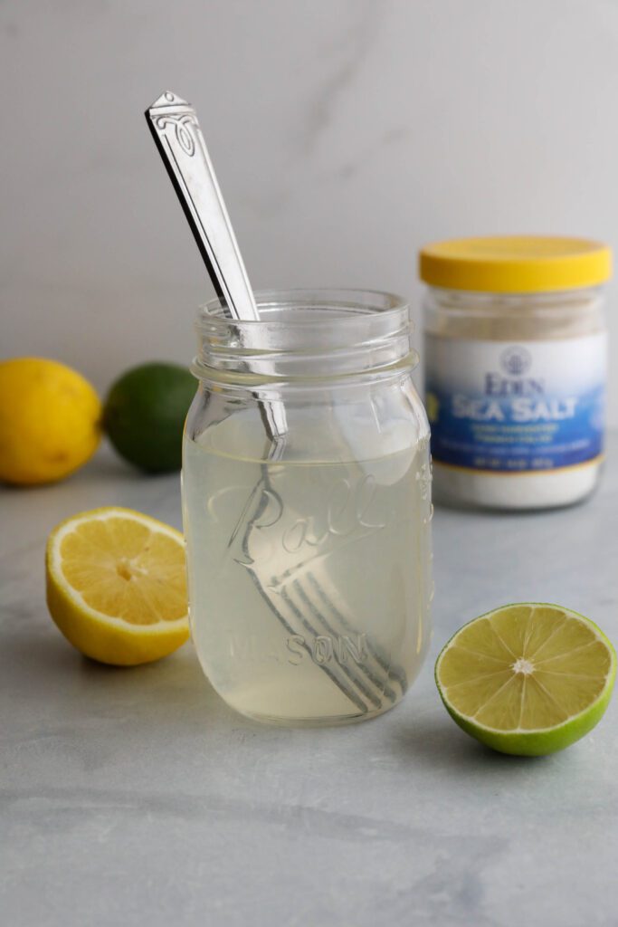 Homemade Electrolyte Water served in mason jar with glass straw and lemons and limes scattered
