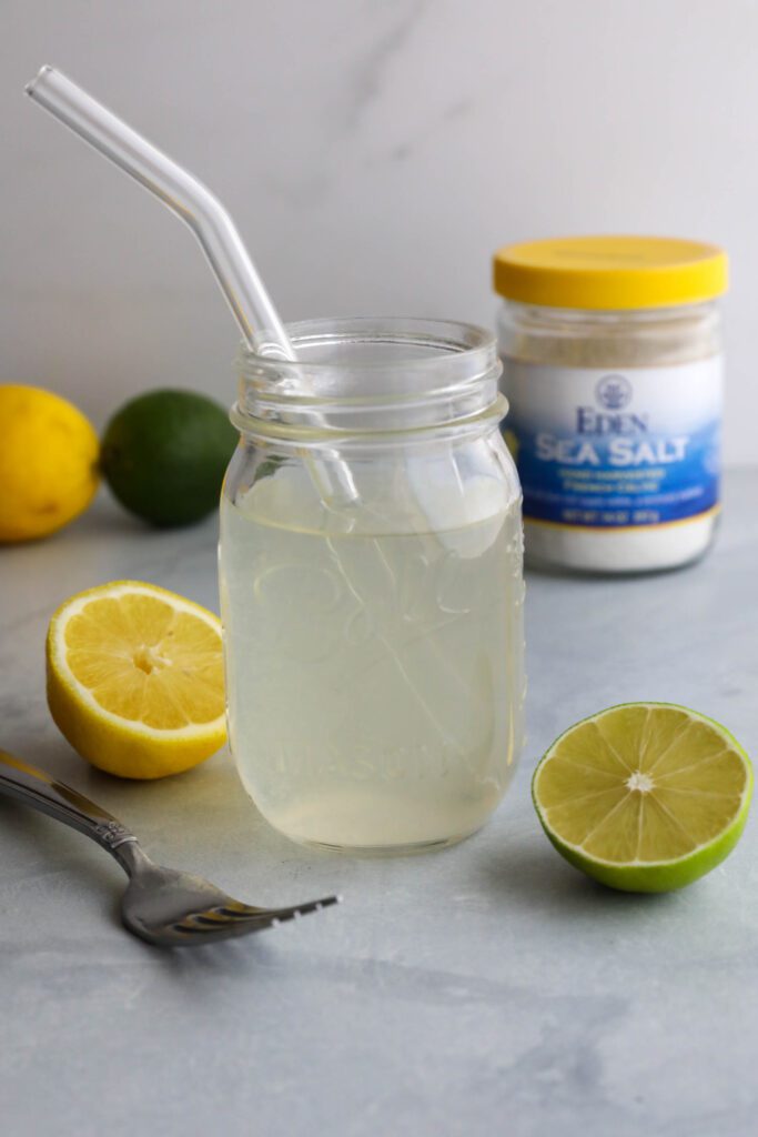 Homemade Electrolyte Water served in mason jar with glass straw and lemons and limes scattered