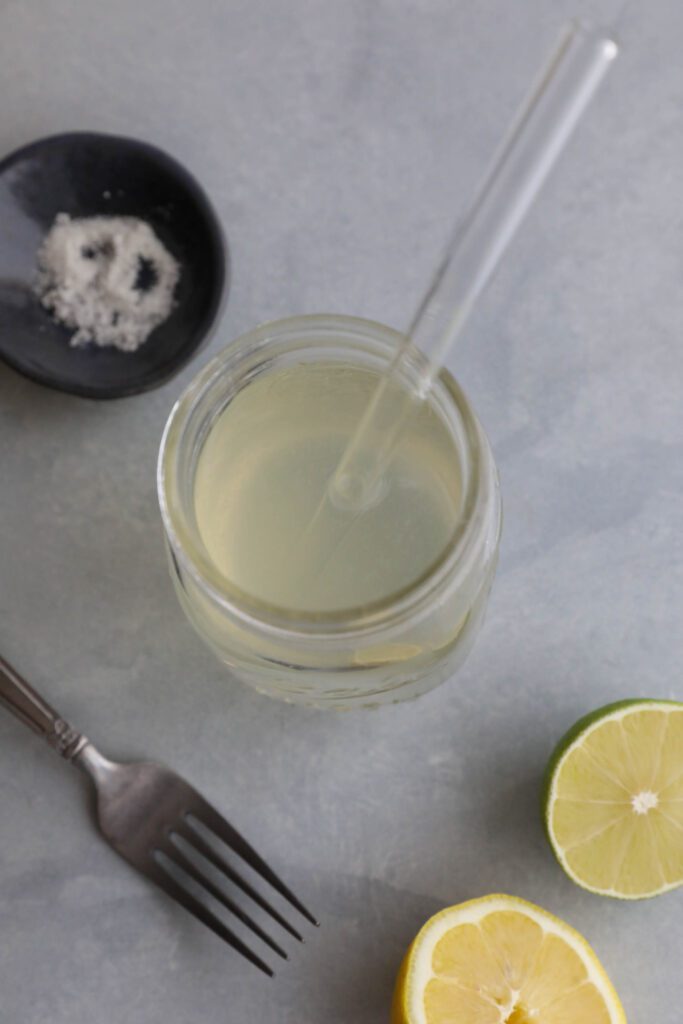 Homemade Electrolyte Water served in mason jar with glass straw and lemons and limes scattered