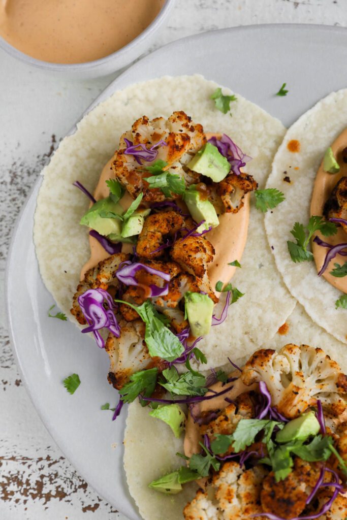 Roasted Cauliflower Tacos served on a plate with Chipotle Cashew Crema topped with cilantro and red cabbage 