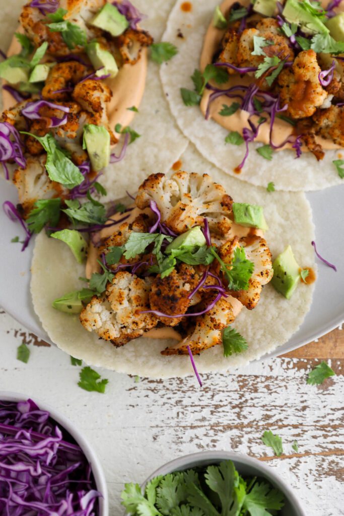Roasted Cauliflower Tacos served on a plate with Chipotle Cashew Crema topped with cilantro and red cabbage 