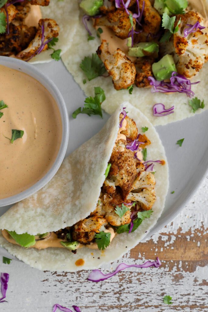 Roasted Cauliflower Tacos served on a plate with Chipotle Cashew Crema topped with cilantro and red cabbage 