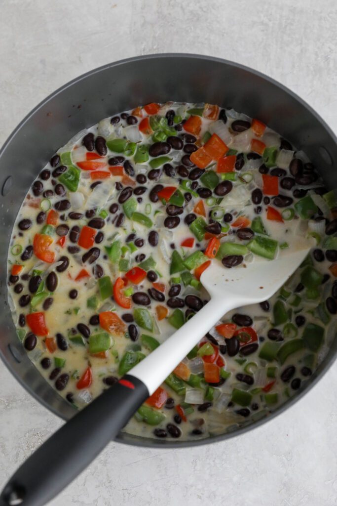 beans, peppers, and onion sin pot with coconut milk and spatula 