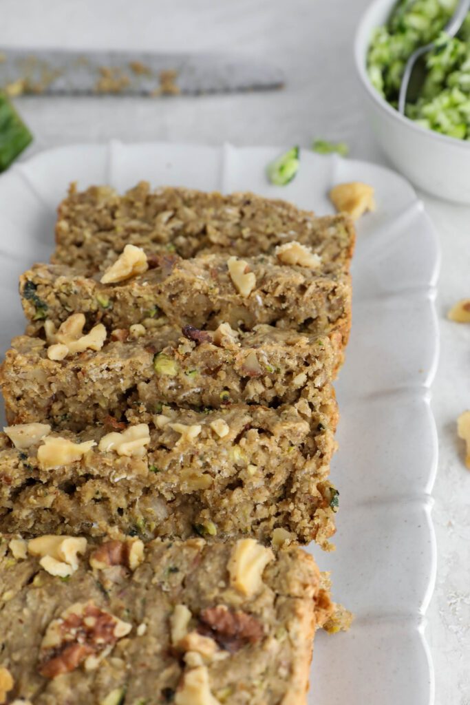 Vegan Zucchini Bread sliced on serving tray with zucchini and walnuts on side.