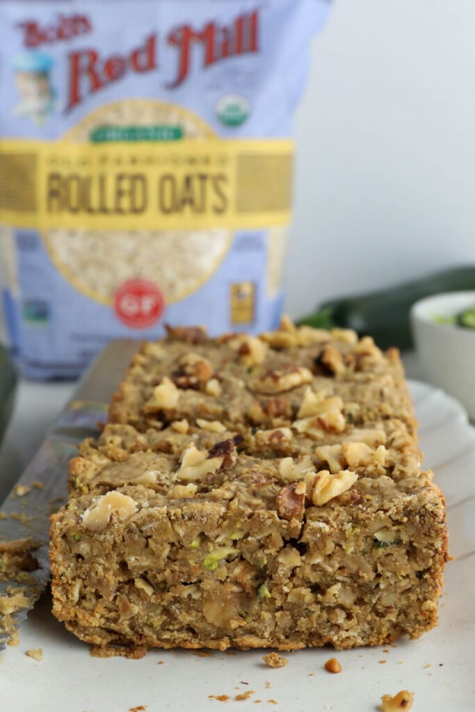 Vegan Zucchini Bread sliced on serving tray with zucchini and walnuts on side. 
