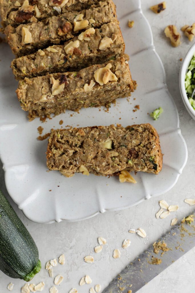 Vegan Zucchini Bread sliced on serving tray with zucchini and walnuts on side. 