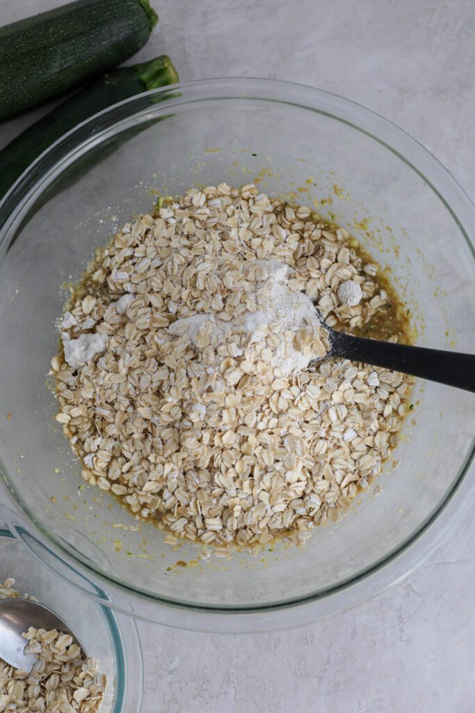 ingredients for zucchini bread in large mixing bowl with spatula and oats on top 