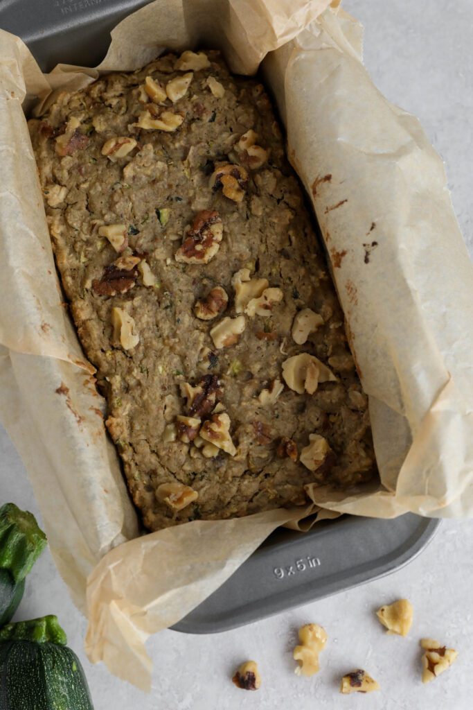 Vegan Zucchini Bread baked in parchment lined loaf pan with zucchini and walnuts on the side