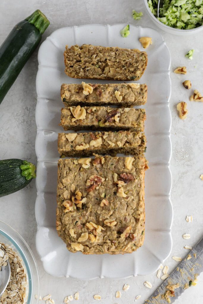 Vegan Zucchini Bread sliced on serving tray with zucchini and walnuts on side. 