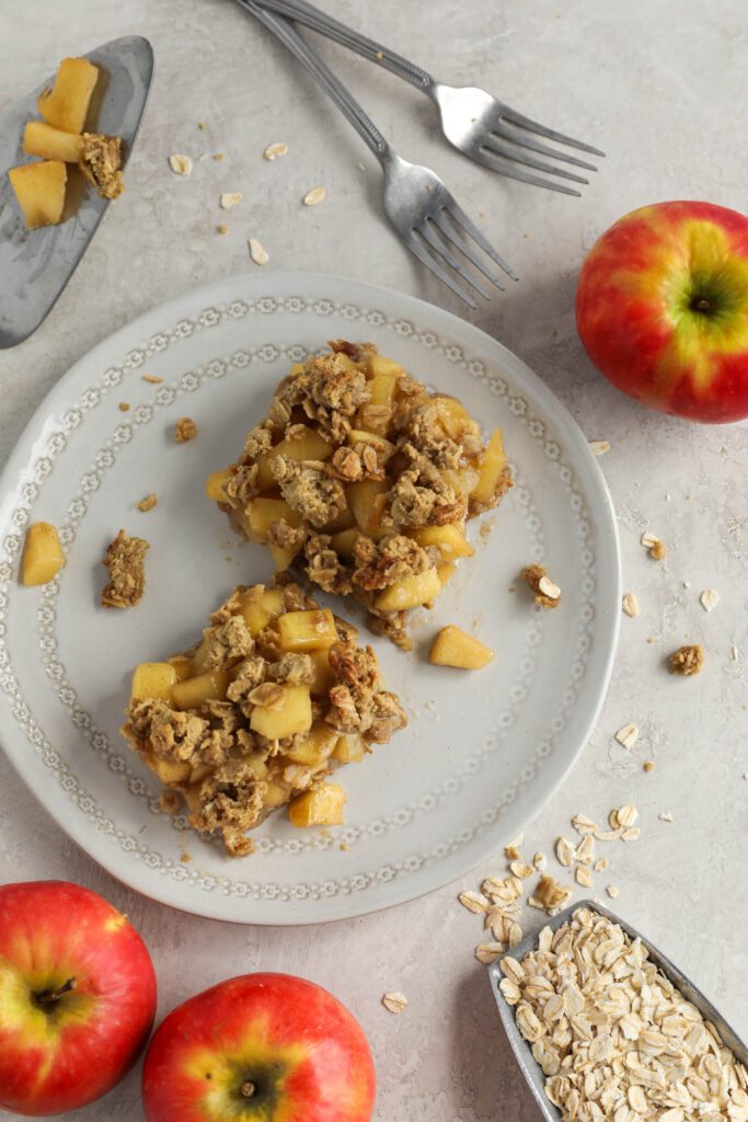 Apple Pie Crumble Bars on white plate with apples on oats on the side and two forks
