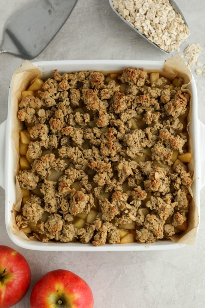 Apple Pie Crumble Bars baked in parchment lined baking dish with oats and apples on the side