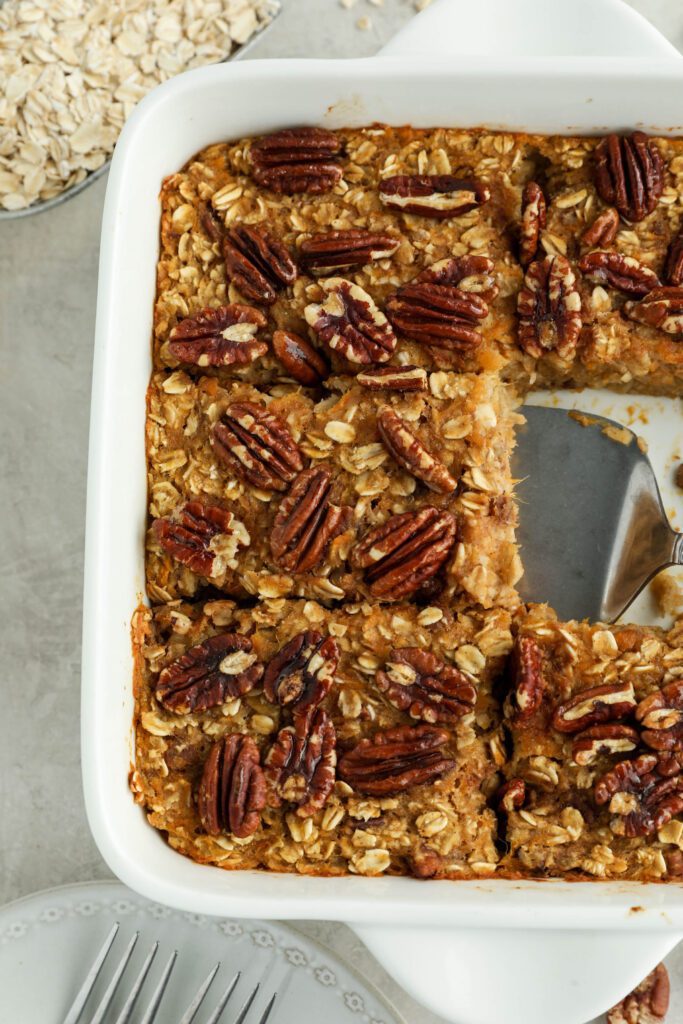 Sweet Potato Pie Baked Oatmeal served in casserole dish with pie server with pecans and oats 